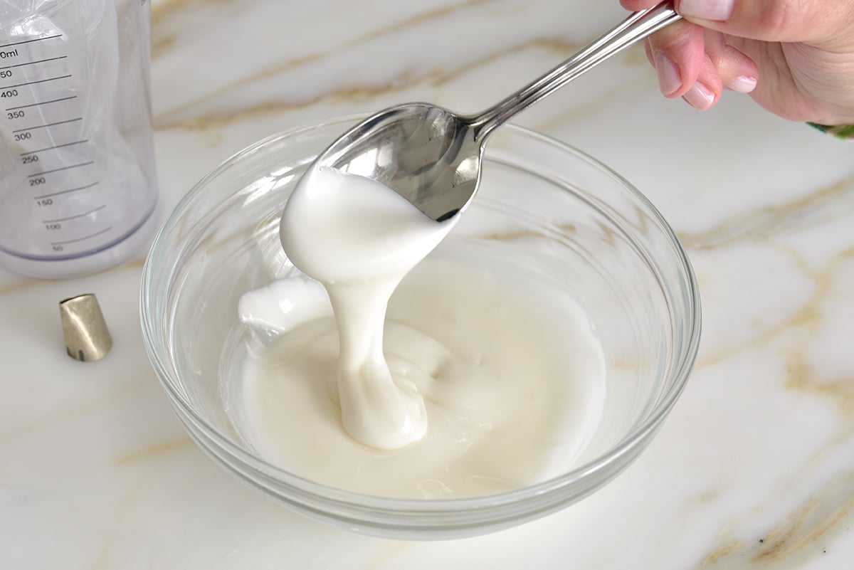 A thick drizzle of white icing falling off a spoon into a glass bowl