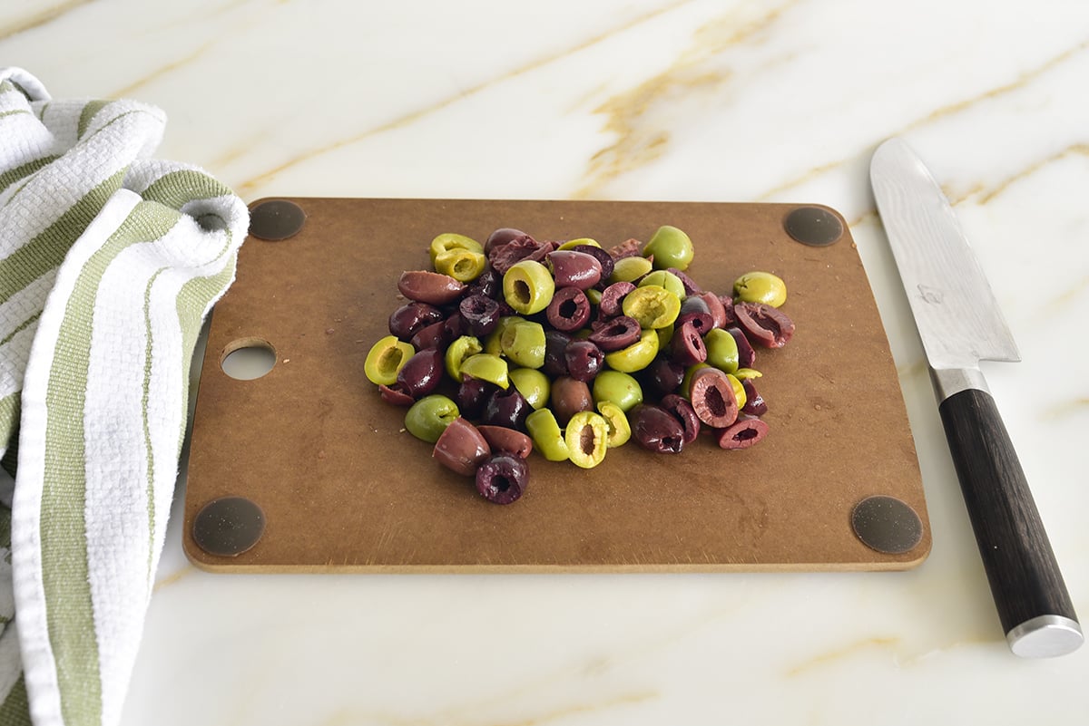 Green and black olives on a cutting board with a knife