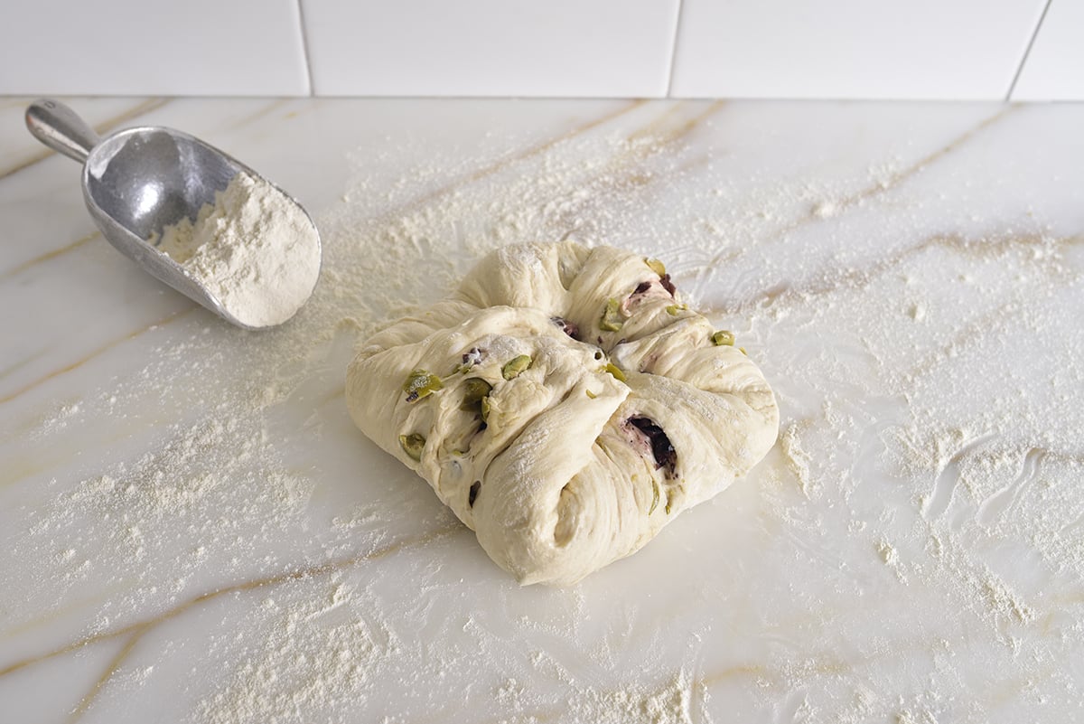 Dough with olives on a marble counter with flour shaped with corners folded into a square