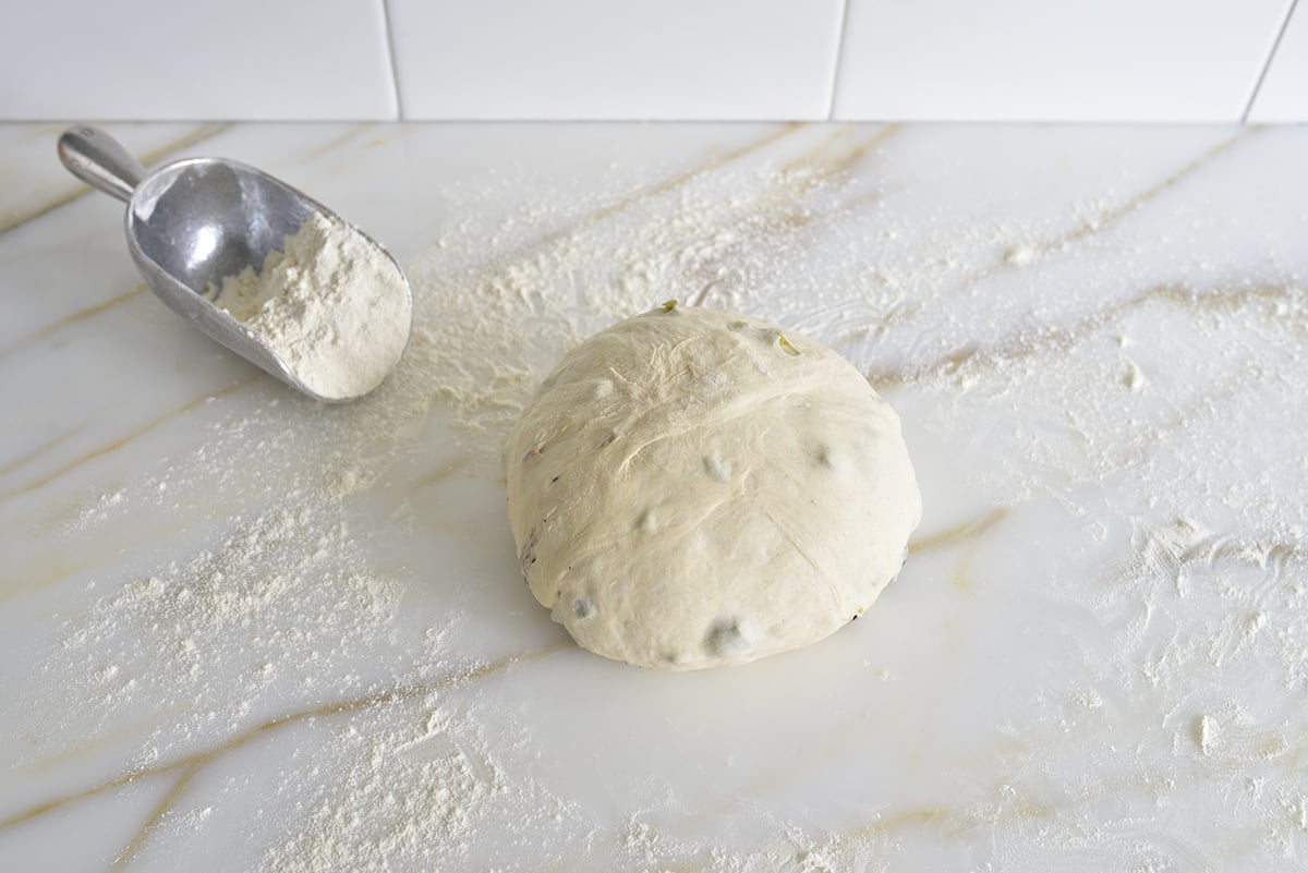 A round dough ball on a floured marble counter