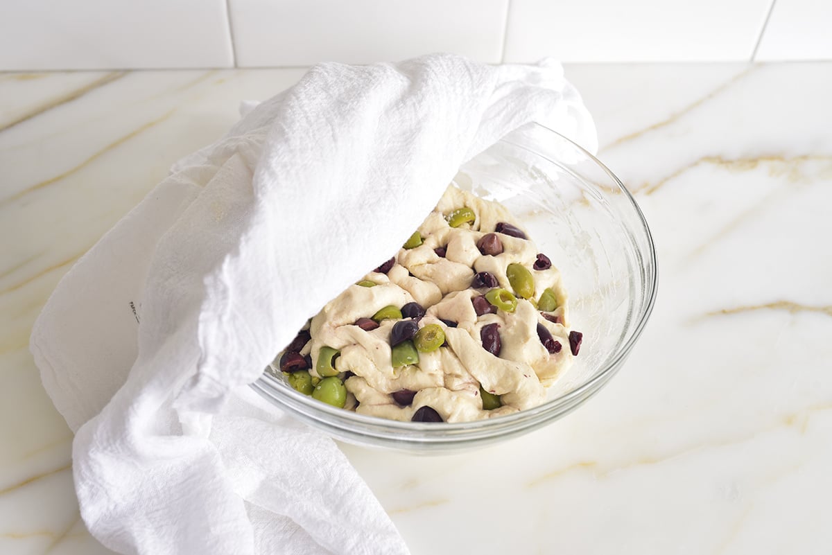 Dough with olives in a  bowl with a towel draped over it