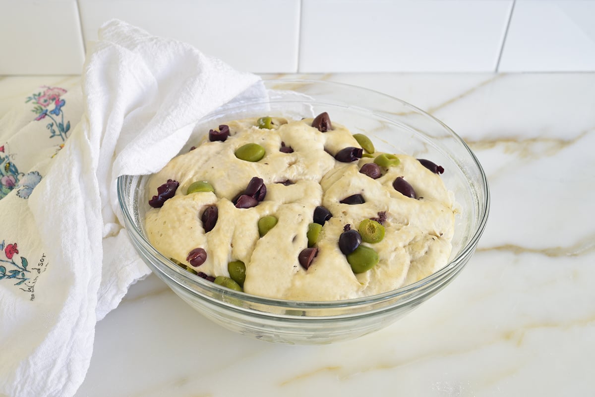 Risen dough with olives in it in a glass bowl