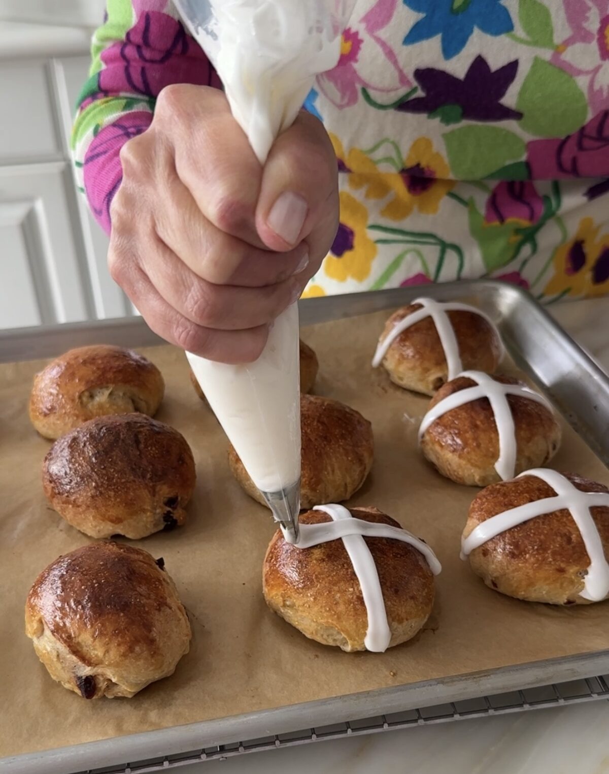 Hands grasping a piping bag to pipe white glaze on a hot cross bun