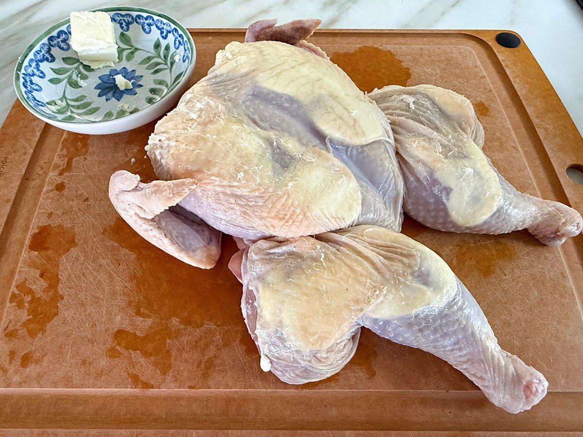 raw chicken with butter under the skin on a board
