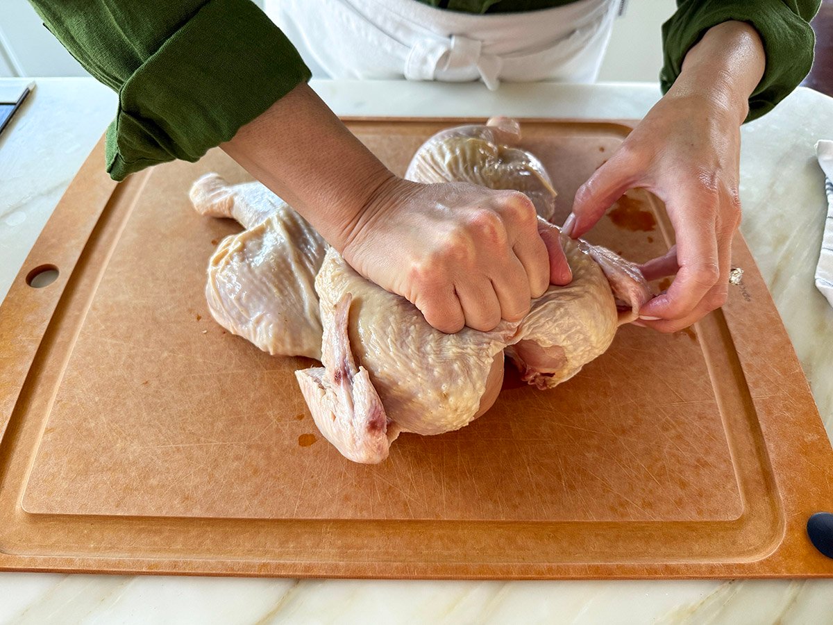 a hand pressing down on the breastbone of a chicken