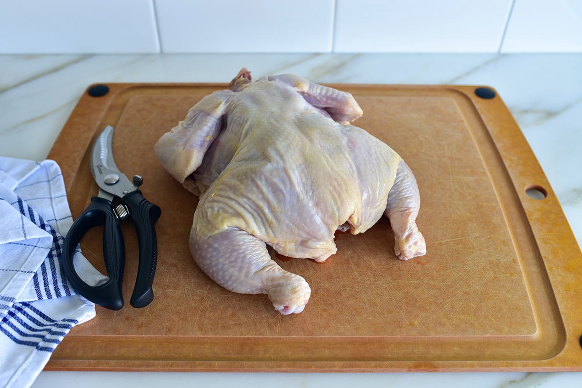 raw chicken on a board with kitchen shears on the side