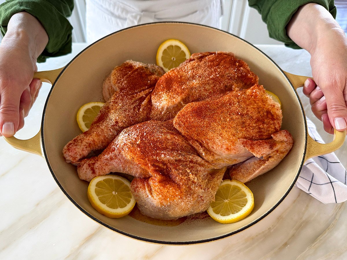 raw chicken coated with spices in a pan with lemon wheels tucked in around it