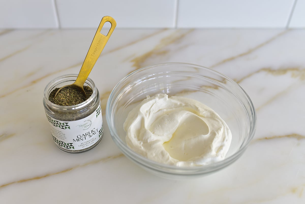 yogurt in a glass bowl with a jar of dried mint next to it