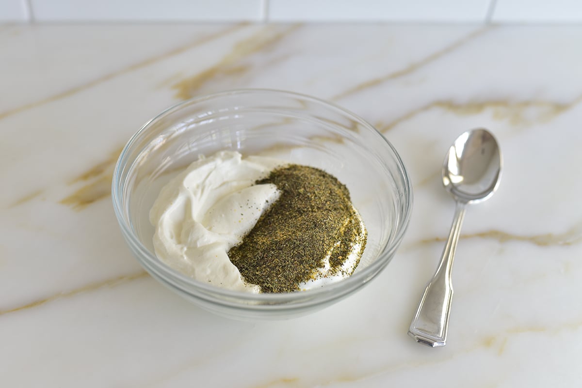 Yogurt with dried mint on top in a glass bowl with a spoon beside it
