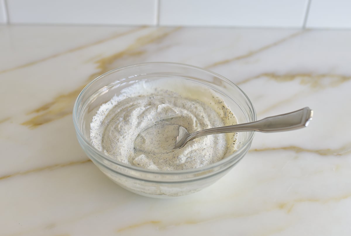 yogurt with flecks of spice in it in a glass bowl with a spoon in it