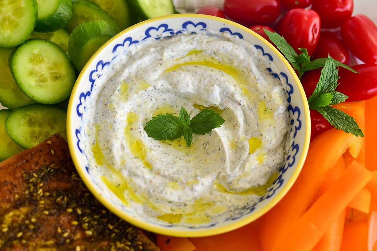 yogurt dip with a mint sprig, olive oil drizzle, and veggies around it