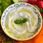 yogurt dip with a sprig of mint in the center and vegetables all around