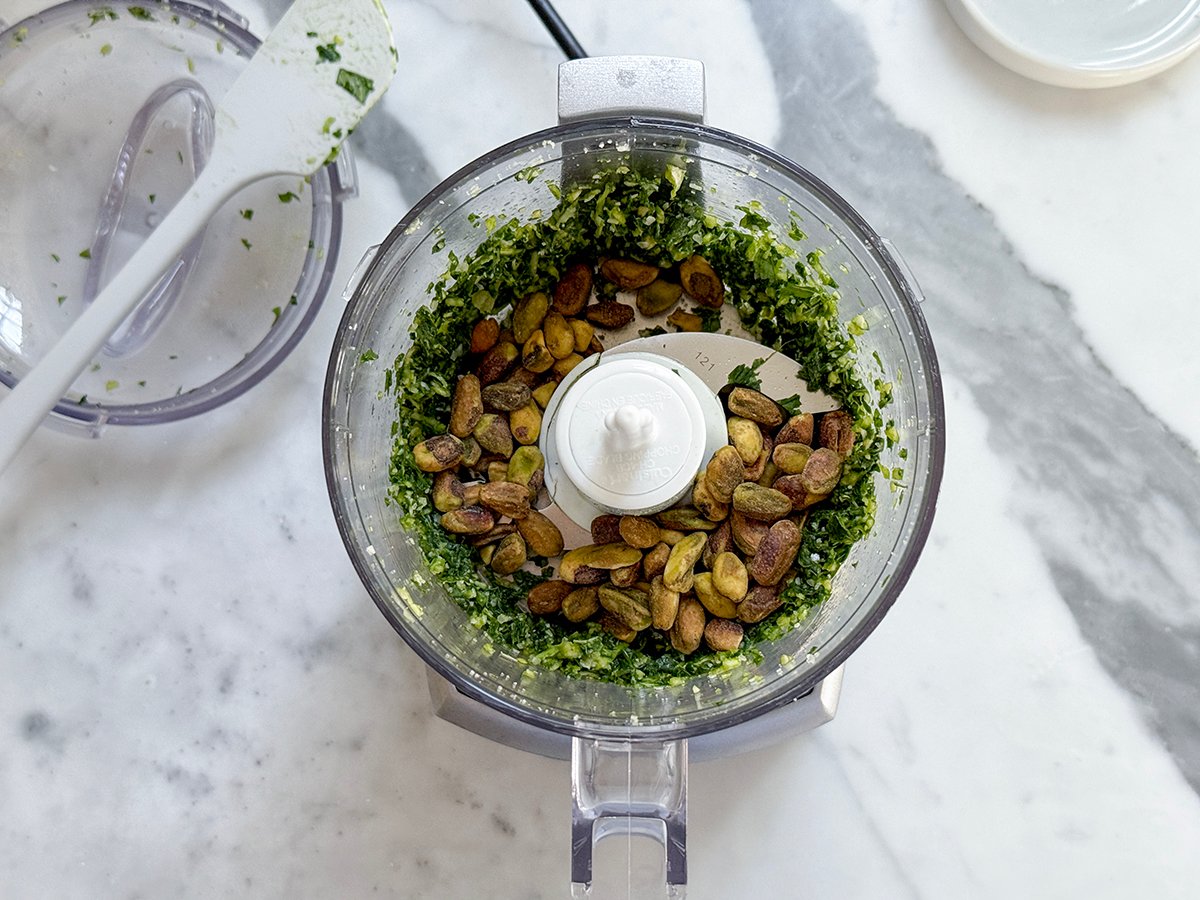 Processor filled with chopped basil and pistachios