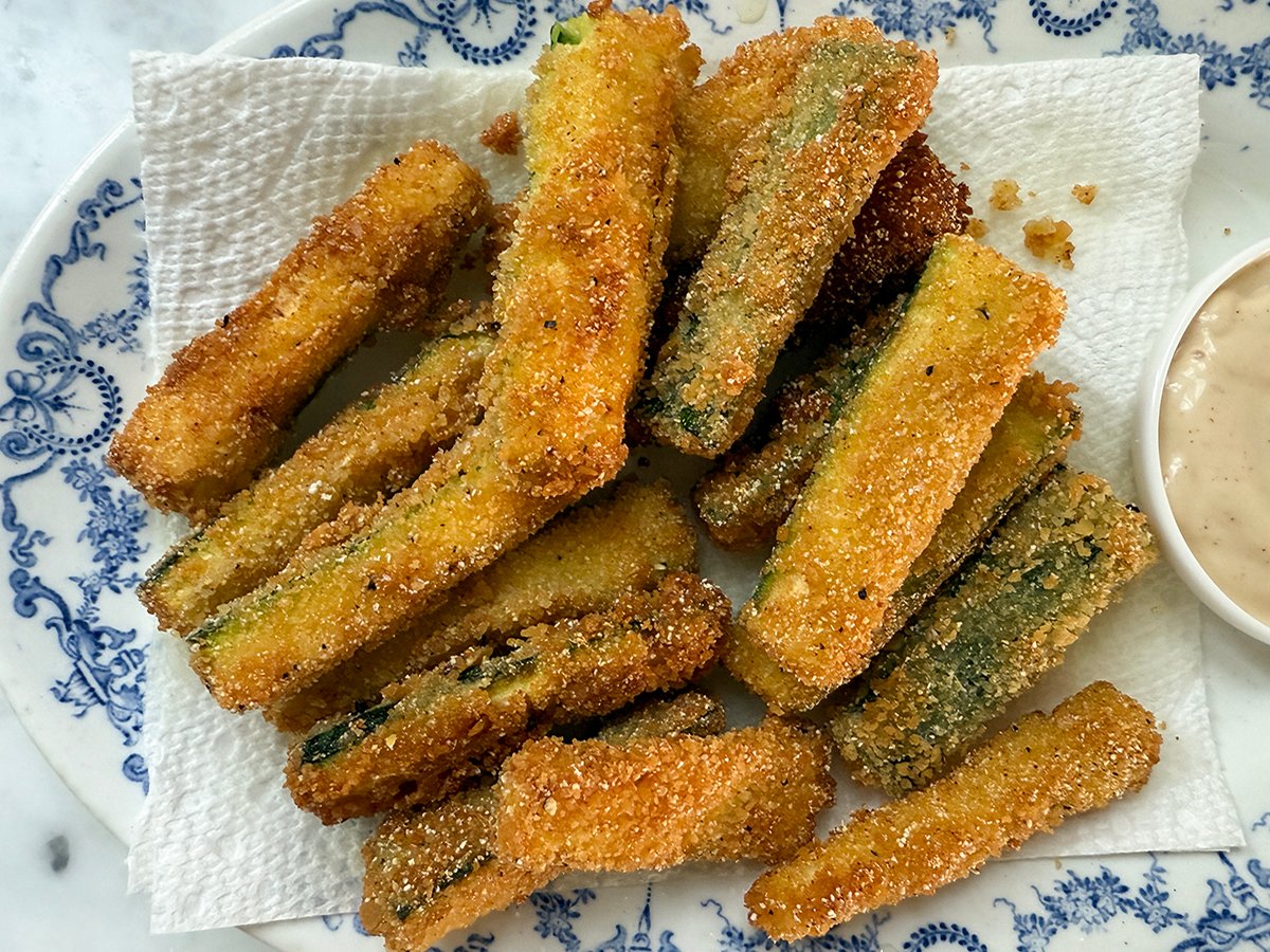 Fried zucchini sticks on a paper towel lined blue and white plate