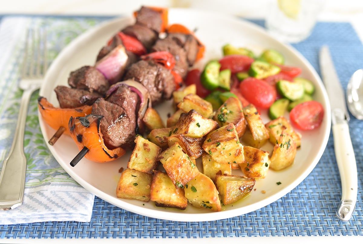 Batata harra on a plate with kebabs and salad