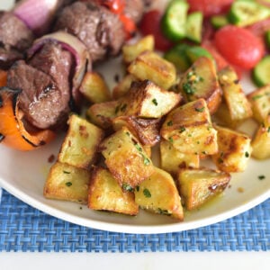 Batata harra potatoes on a white plate with kebabs and salad