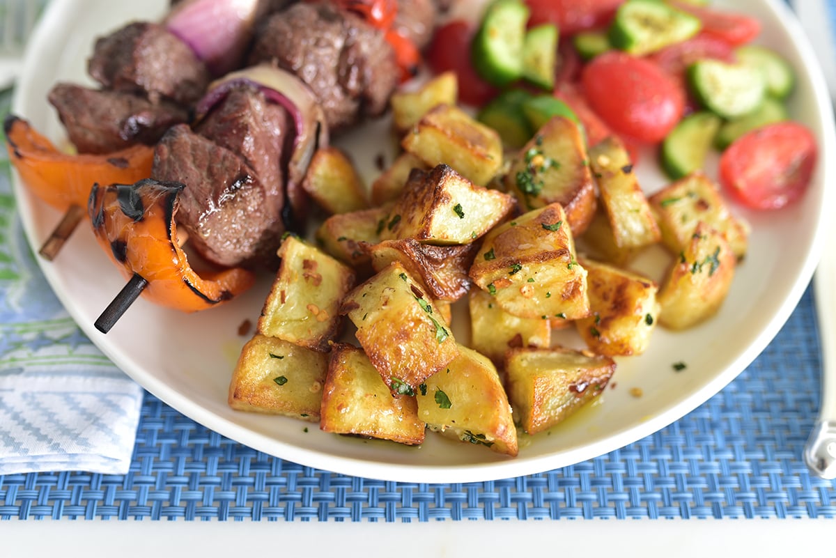 Batata harra potatoes on a white plate with kebabs and salad