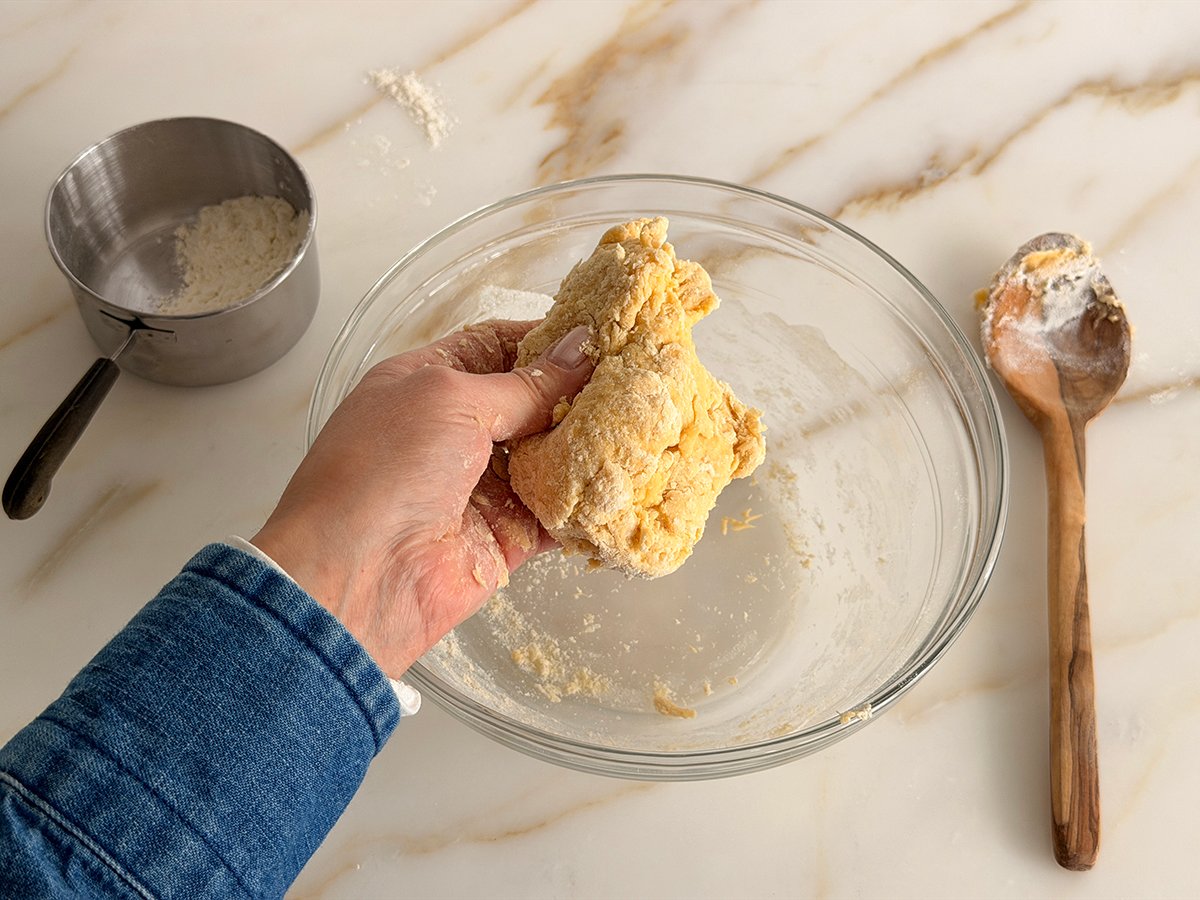 a hand with a blue sleeve holding initially kneaded egg noodle dough