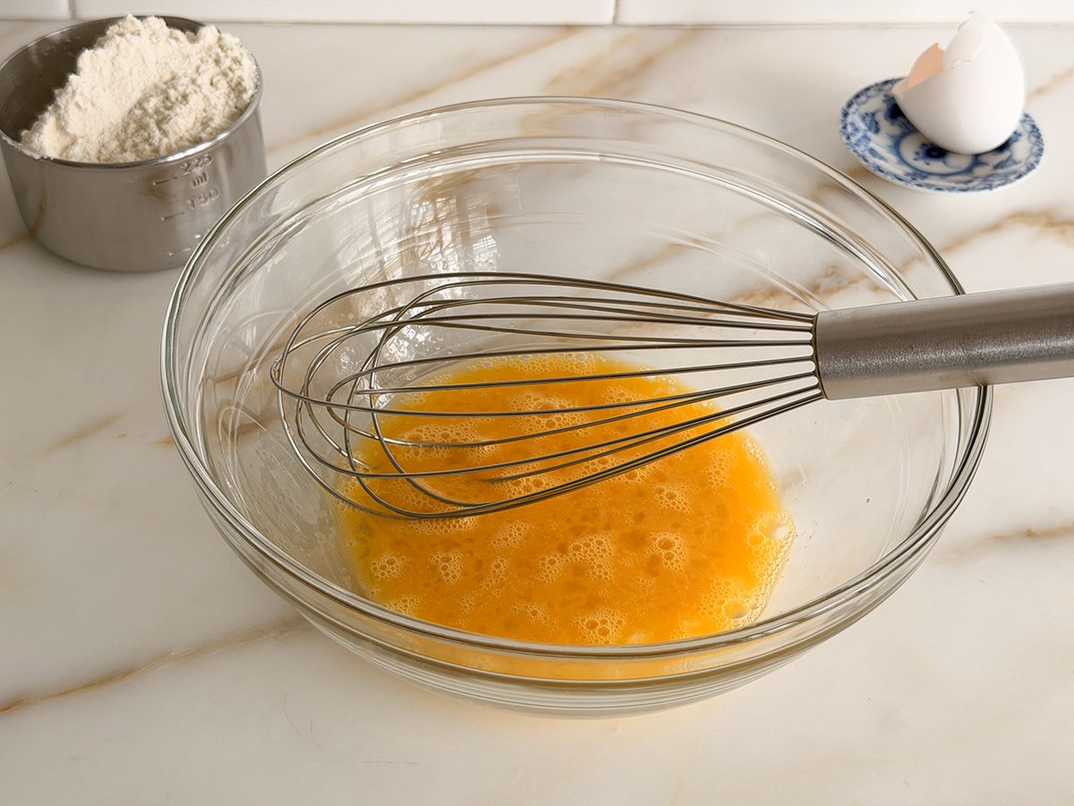 Eggs in a glass bowl with a whisk in it