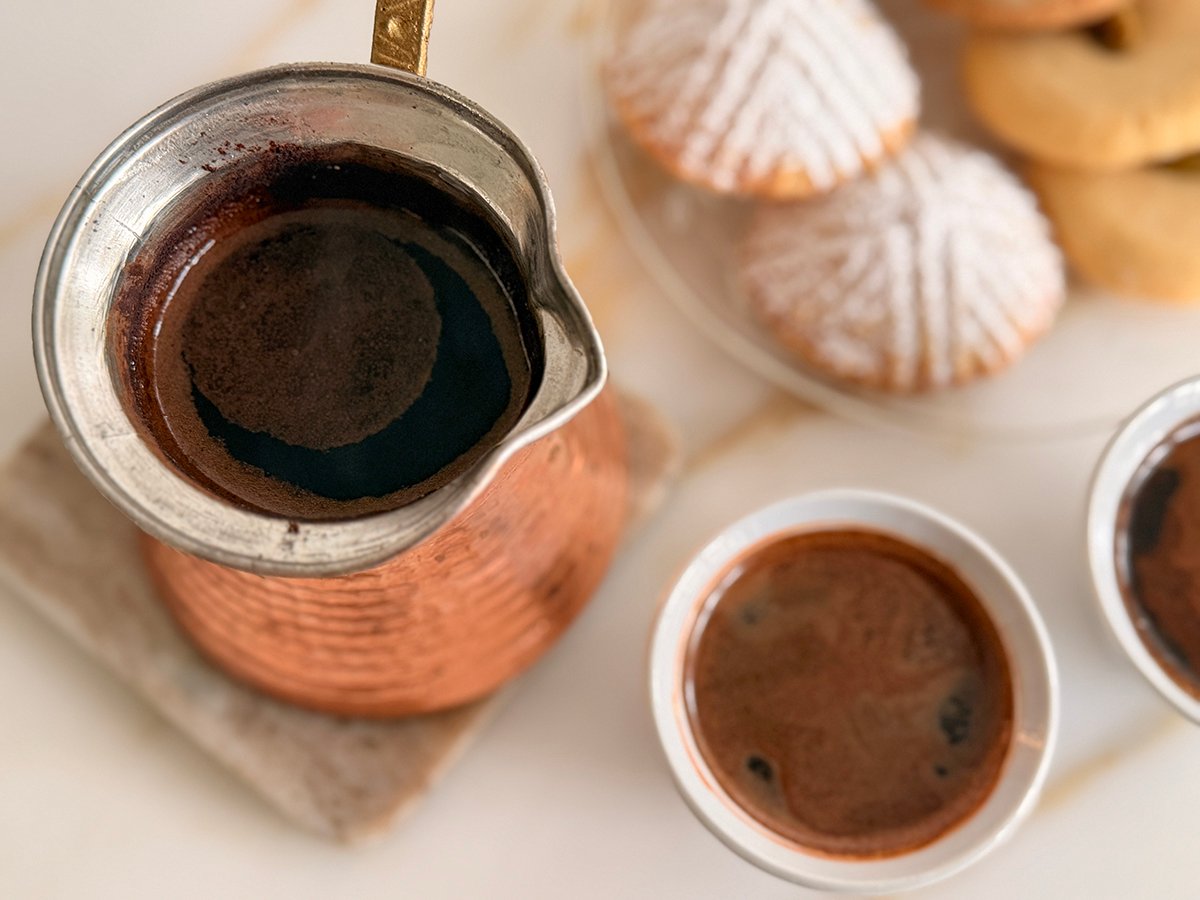 Arabic coffee in a copper pot with a cup on the side and two mamoul cookies