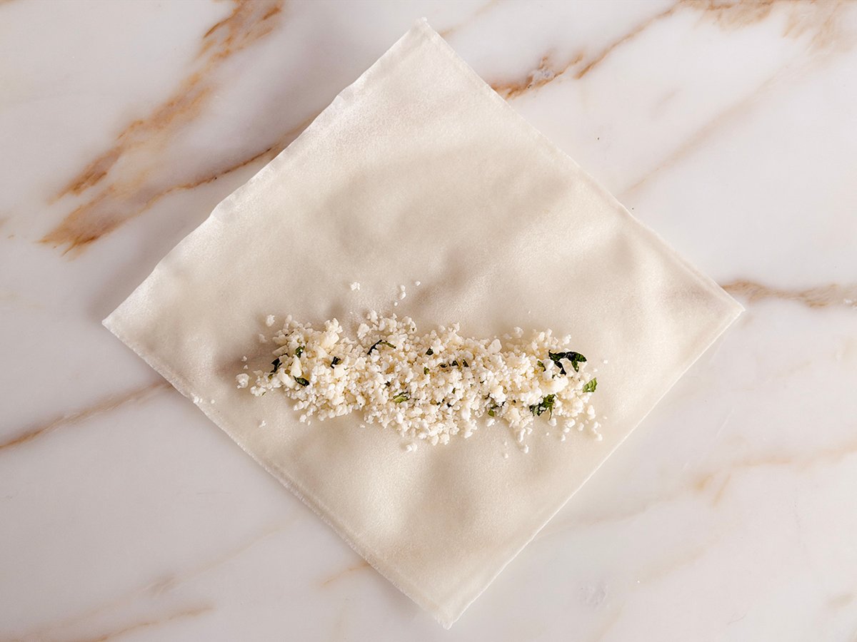 spring roll wrapper on the counter showing step one with cheese filling across the center