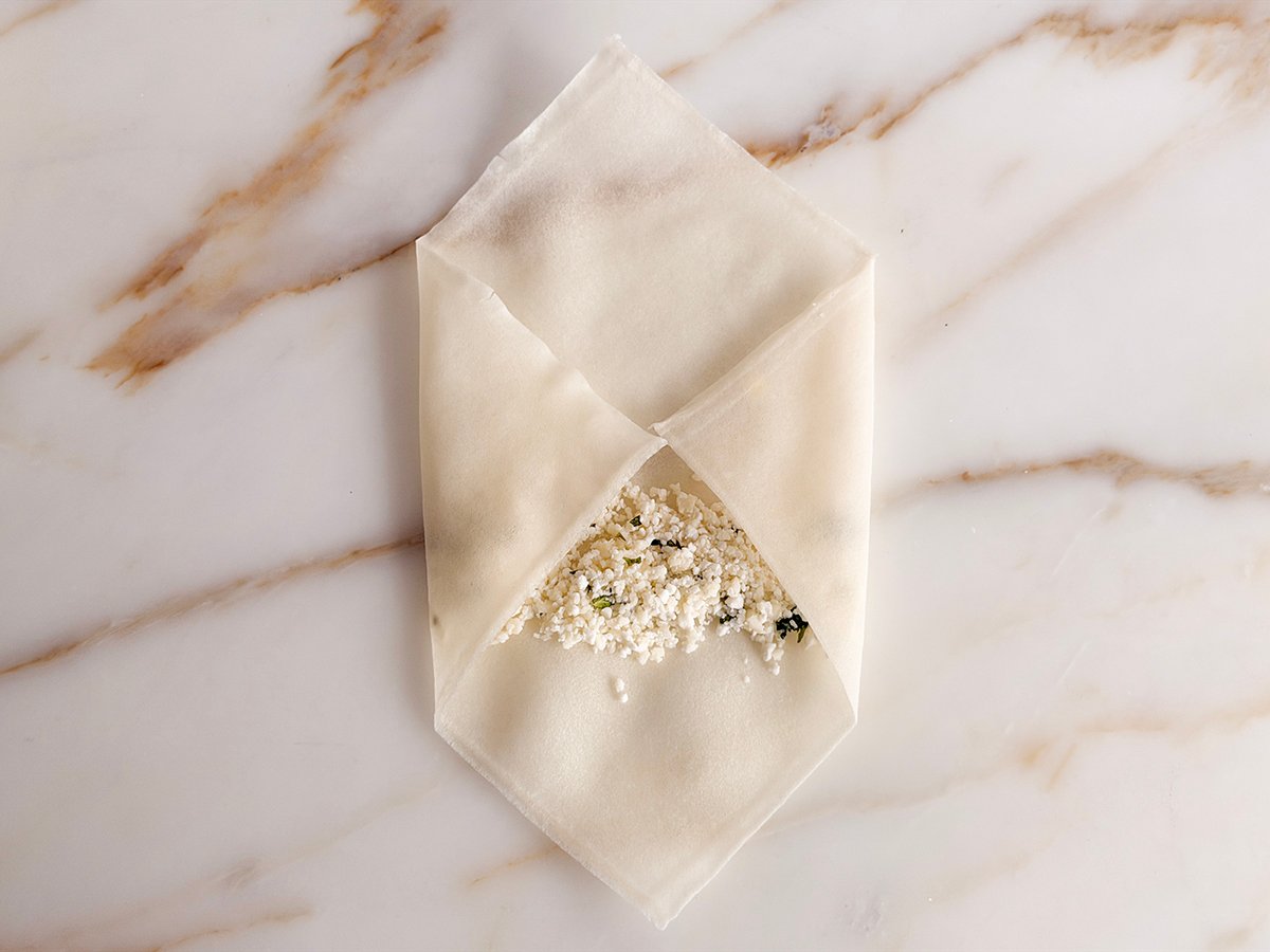 spring roll wrapper on the counter showing step two with left and right sides folded over cheese filling 