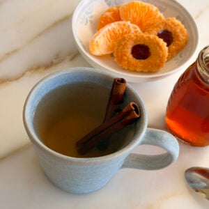Cinnamon tea in a blue mug with a plate of oranges and cookies on the side