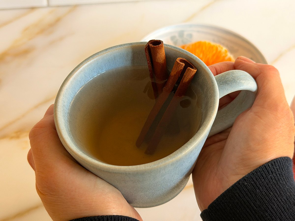 A blue mug of cinnamon tea in two hands