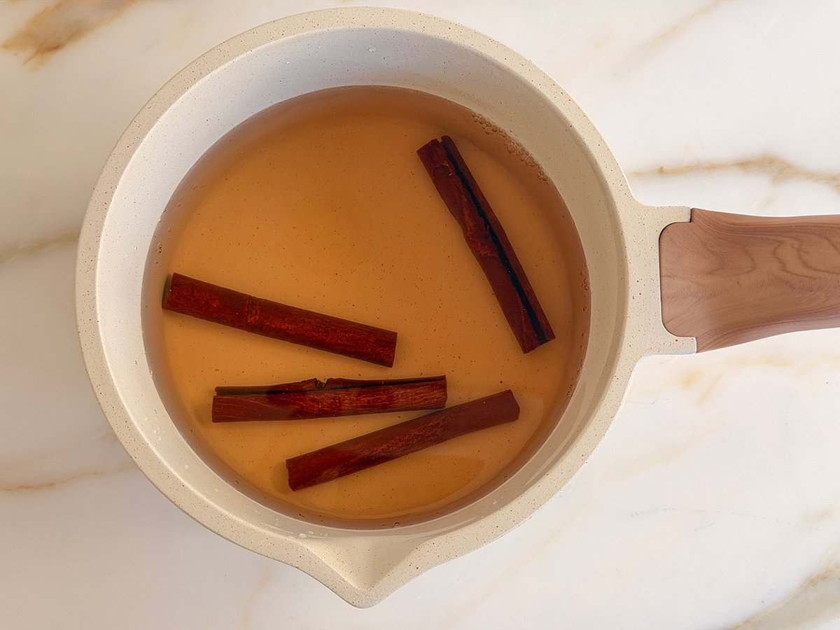 A white pot holding infused water and floating cinnamon sticks