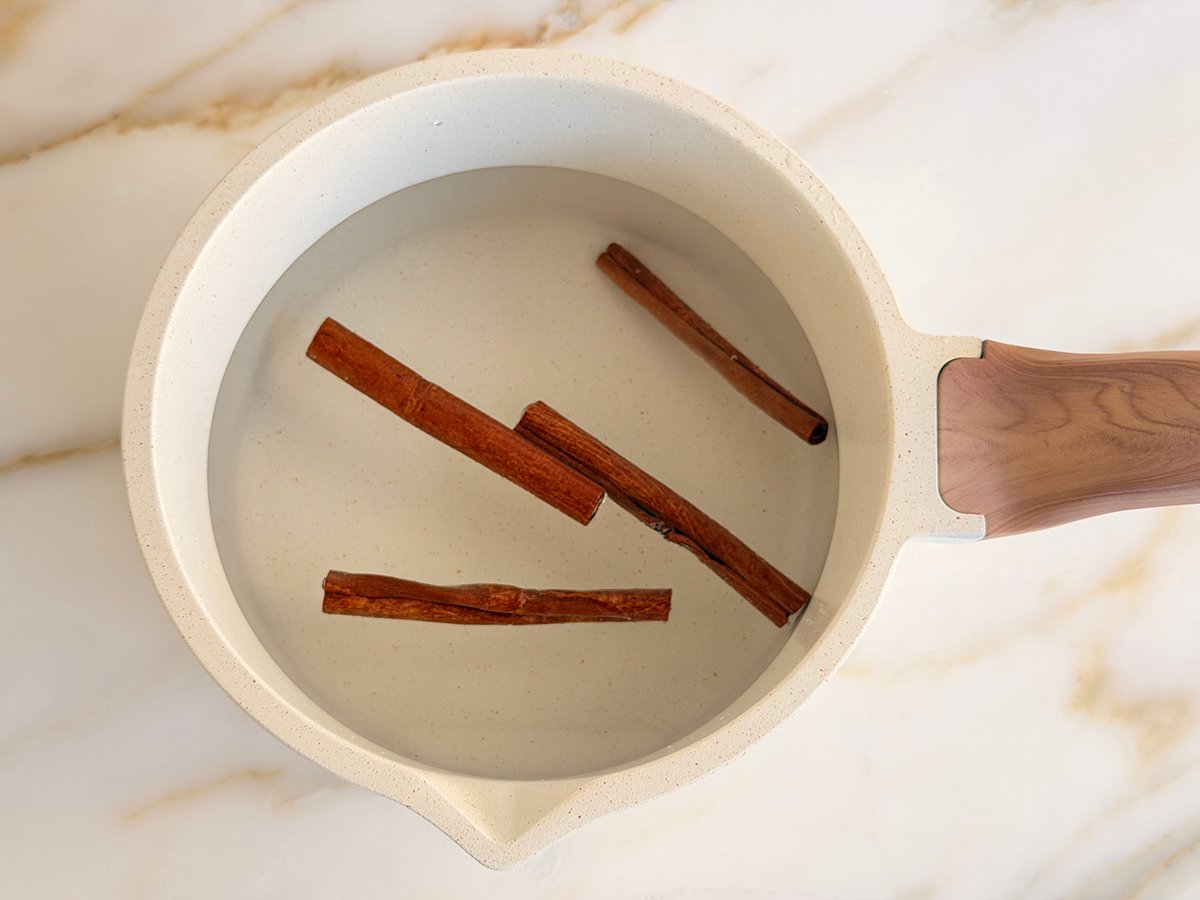 A white pot holding water and floating cinnamon sticks