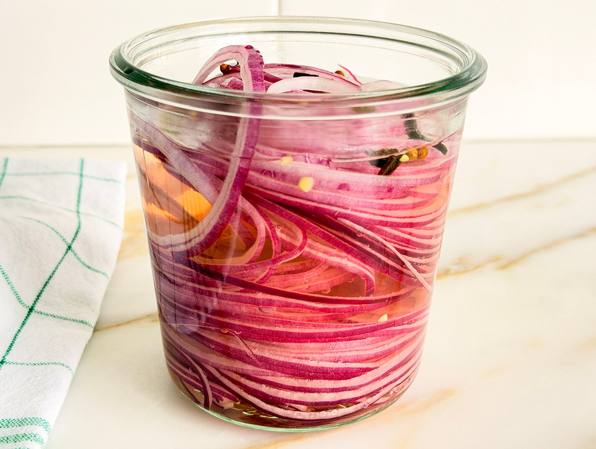 Glass jar of sliced red onions in pickling liquid