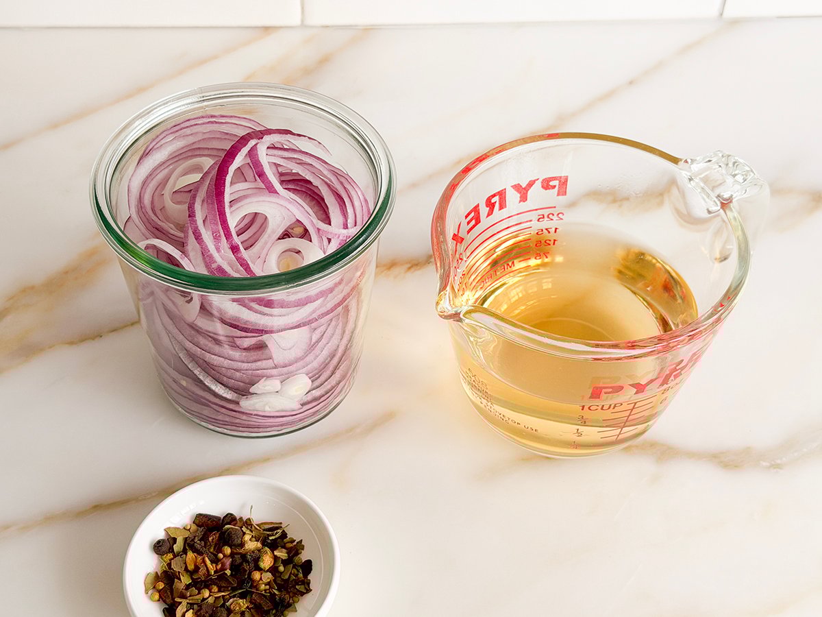 Red onions in a jar beside a glass measuring cup with amber liquid in it