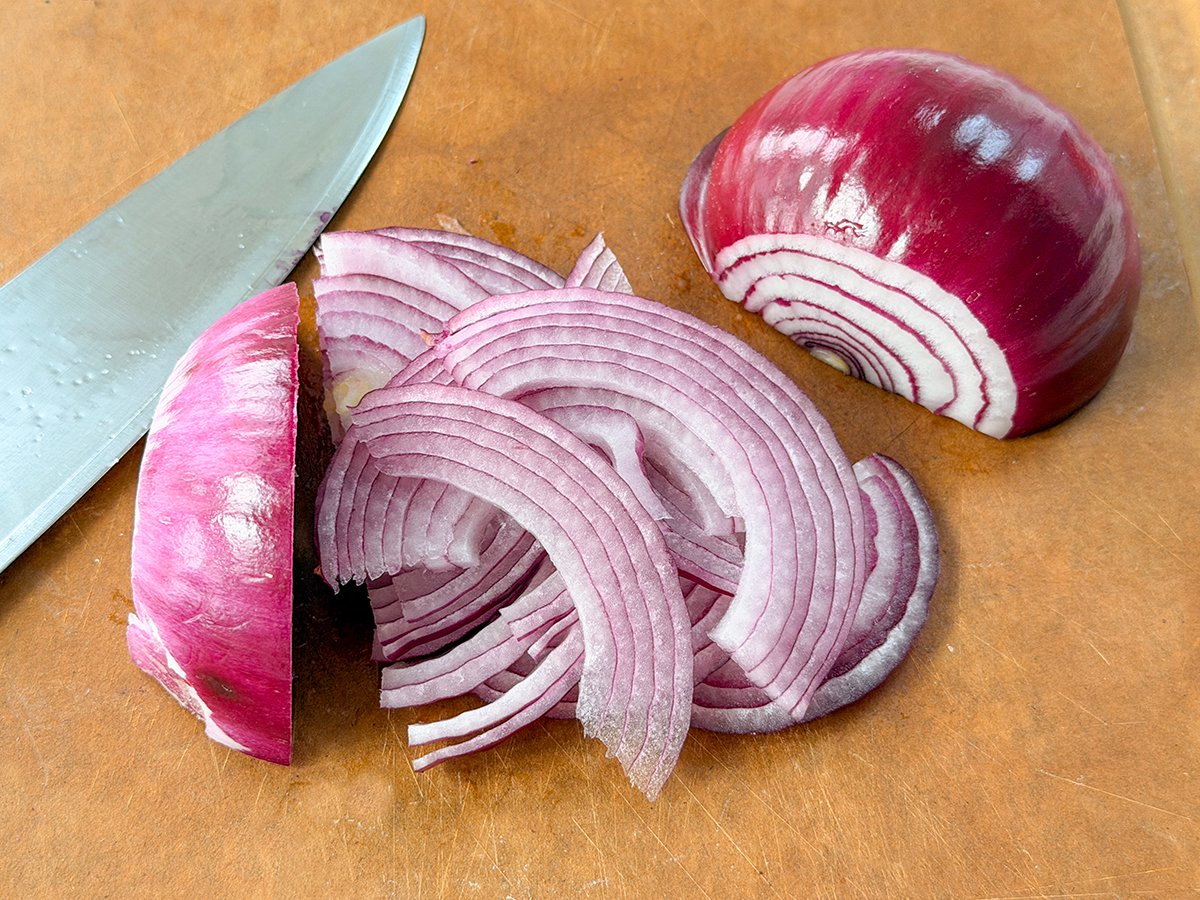 Slices of red onion on a cutting board with a knife