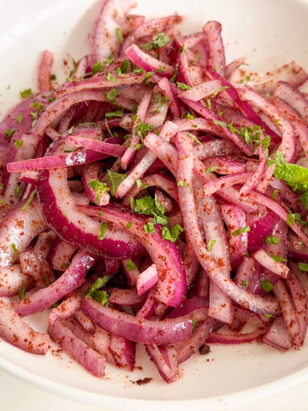 Sumac onions in a white bowl with a mint sprig on the side