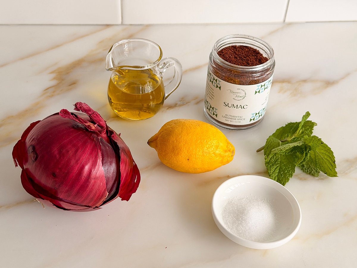Ingredients for sumac onion salad on a marble countertop