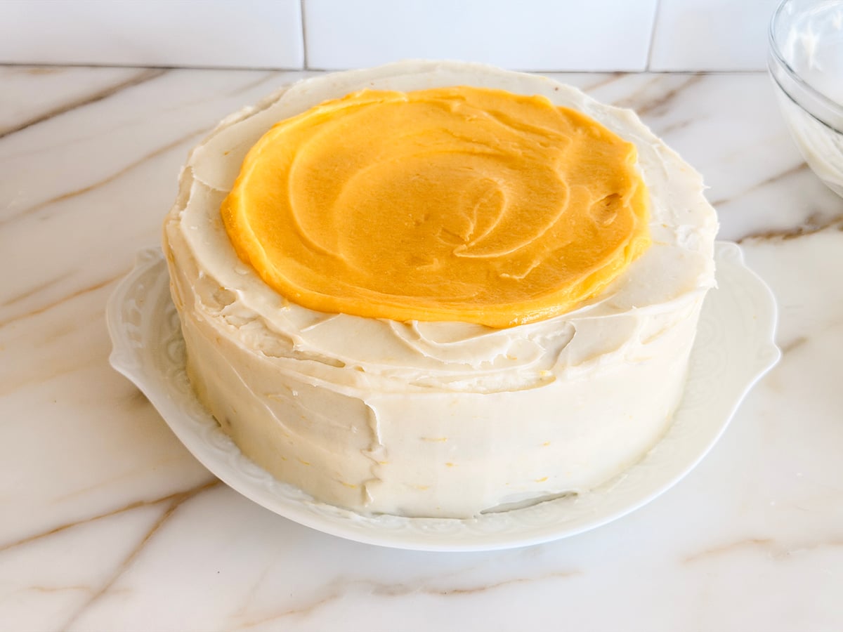 Lemon curd spread over the top of a white frosted layer cake