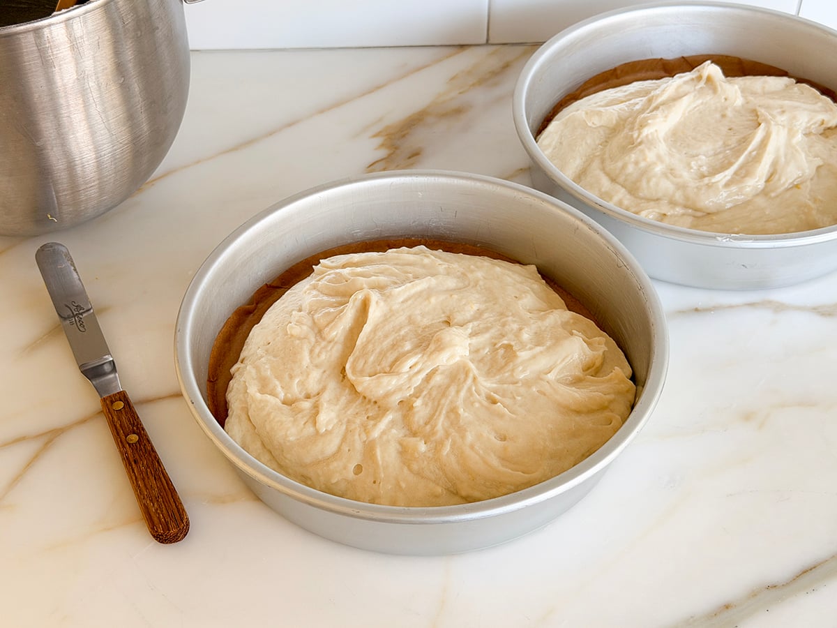 Batter in two cake pans with an offset spatula on the side