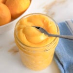 lemon curd in a jar with a spoon in it and a blue towel in the background