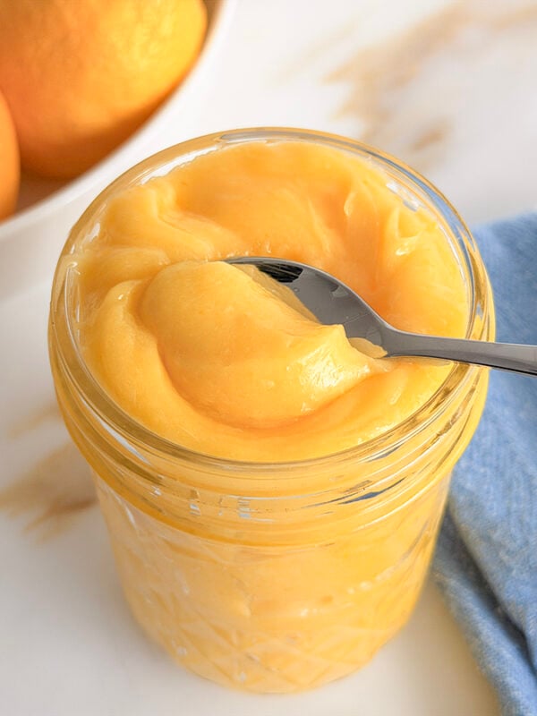 lemon curd in a jar with a spoon in it and a blue towel in the background