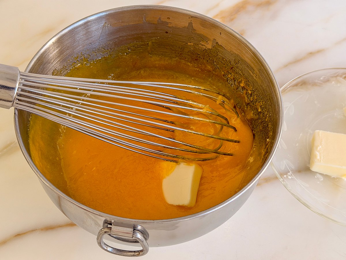 A metal bowl with whisk and a pat of butter in lemon curd