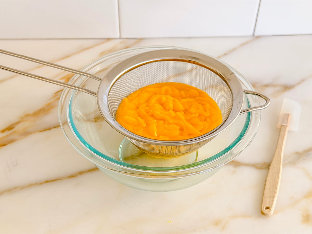 lemon curd in a metal strainer set over a glass bowl