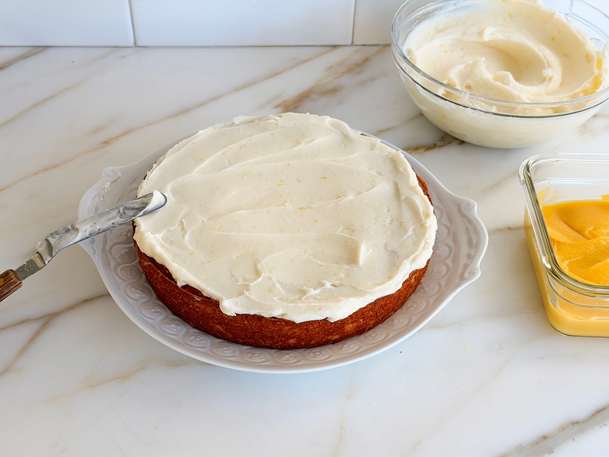 One layer of cake spread with buttercream with bowl of frosting and bowl of lemon curd on the side