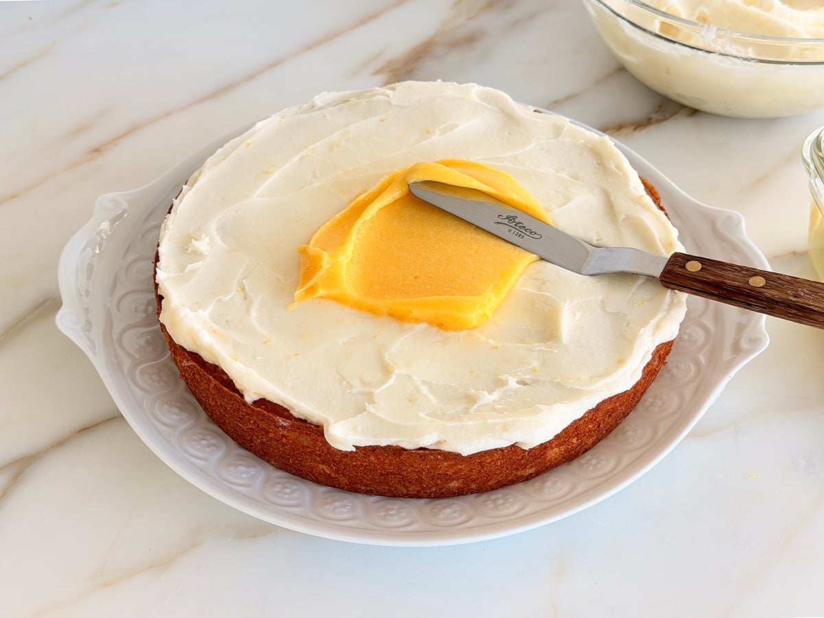 One layer of cake spread with buttercream and a dollop of lemon curd with an offset spatula on top