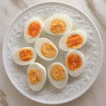 White plate with halved boiled eggs on a marble countertop.