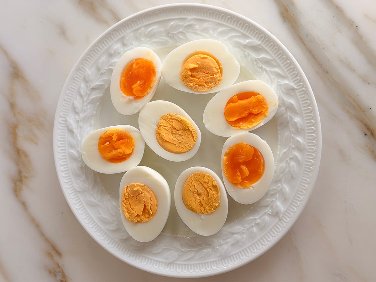 White plate with halved boiled eggs on a marble countertop.
