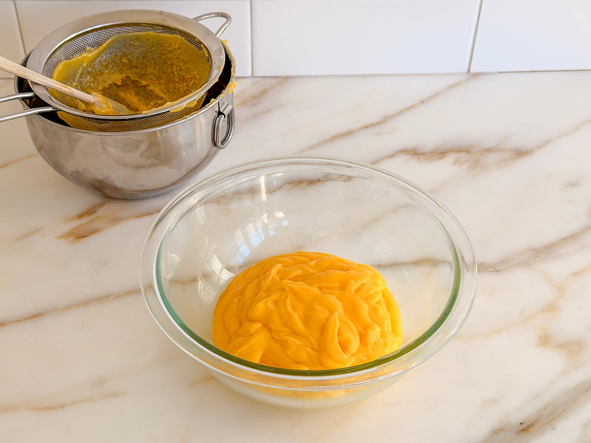 lemon curd in a glass bowl with a strainer on the side