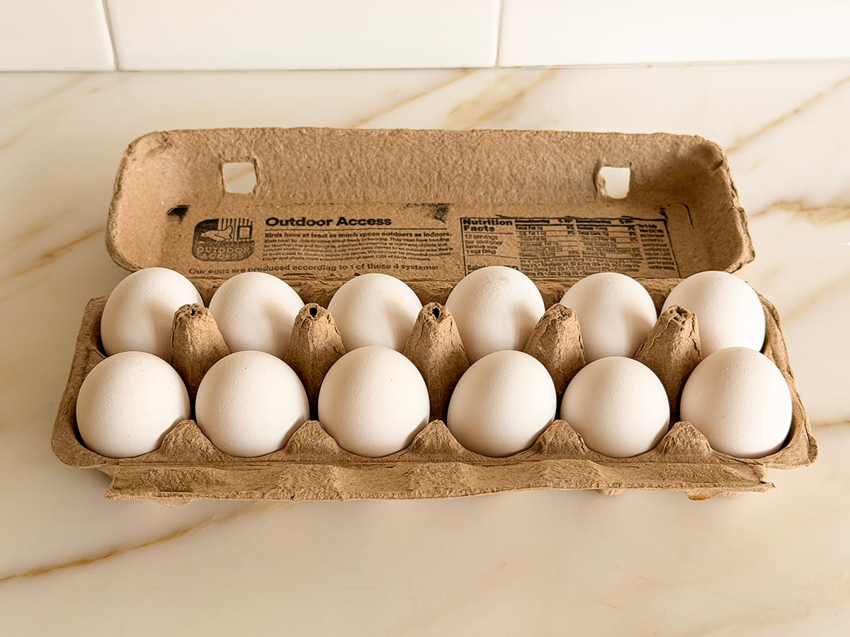 Dozen eggs in a cardboard container on a marble surface.