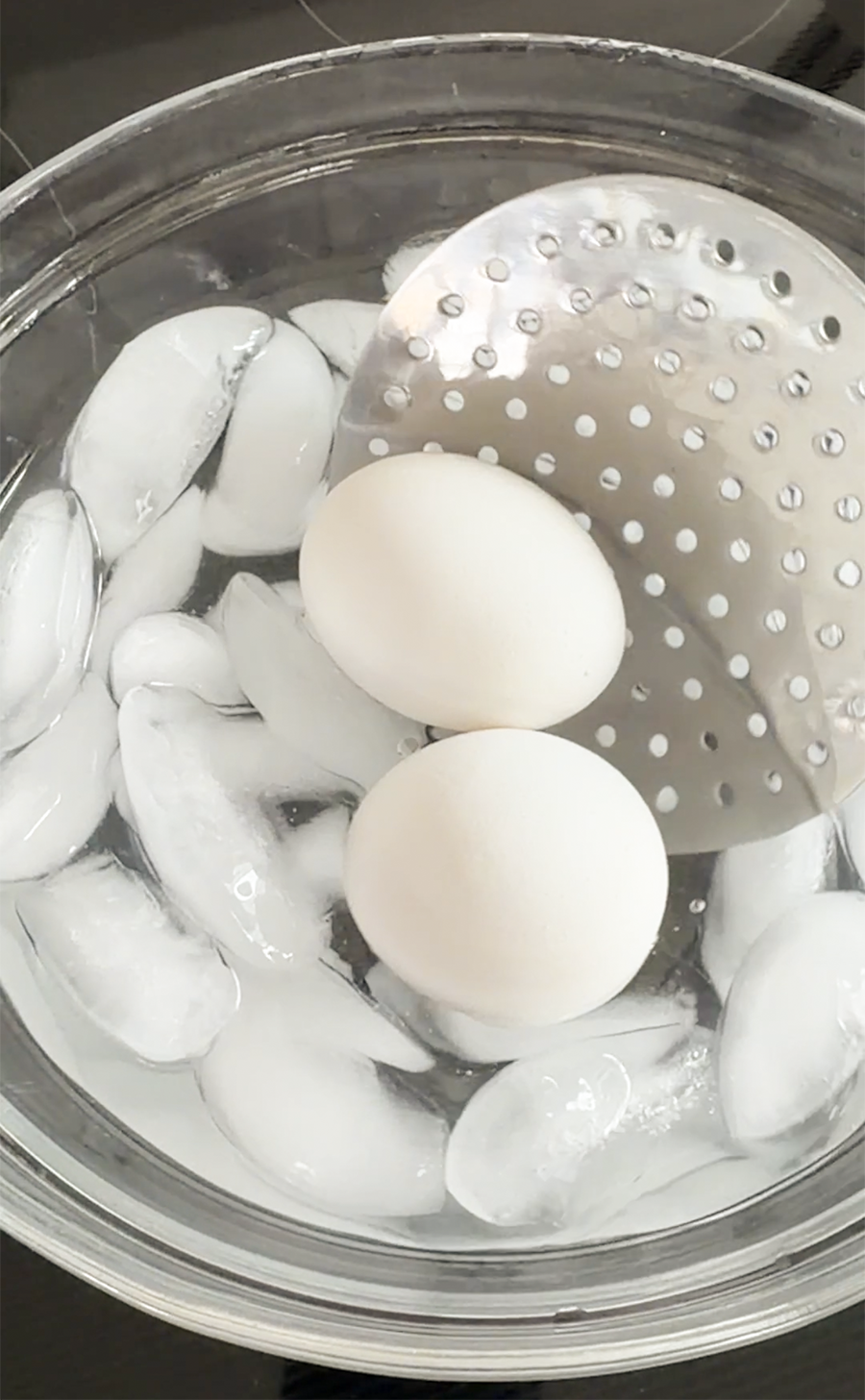 Eggs being added to ice water in a bowl with a slotted spoon.