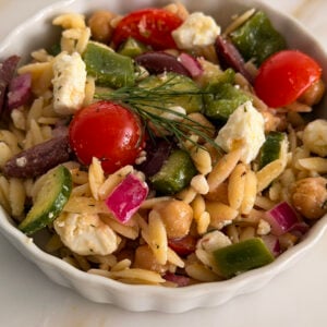 Greek orzo pasta salad in a white bowl with dill on top