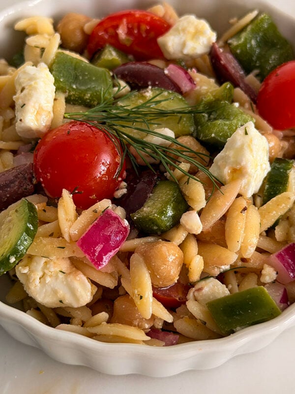 Greek orzo pasta salad in a white bowl with dill on top